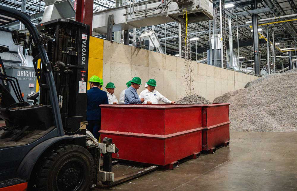 Group of men wearing safety vests and hard hats standing inside a plastics renewal facility.